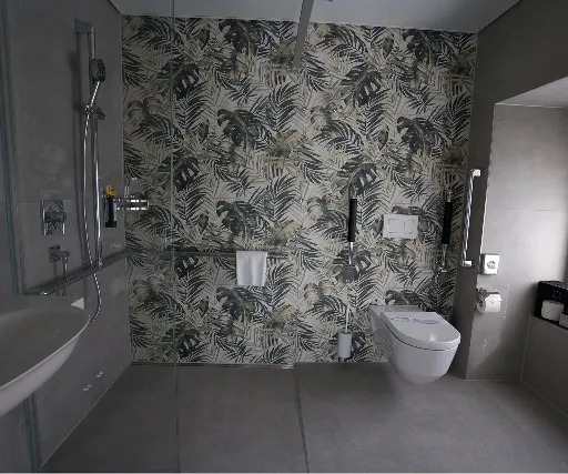 Hotelbad mit Wandplatten im Blattmuster, Haltegriffen und bodenebener Dusche.