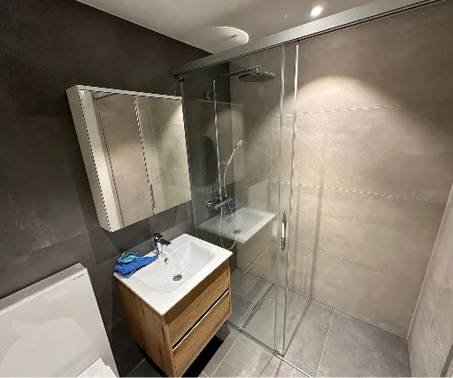 Duschbad mit Glasschiebetür, bodenebener Dusche und grossformatigen Platten.
