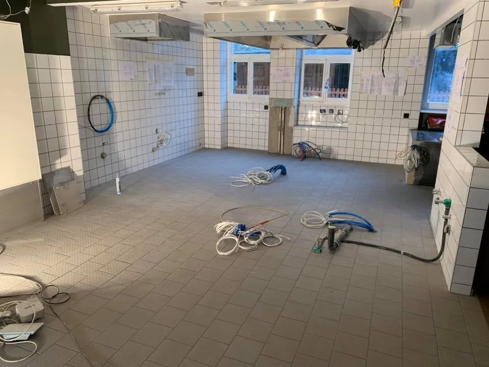 Gastroküche mit weiss geplatteten Wänden, Dunstabzug und offenen Installationen.