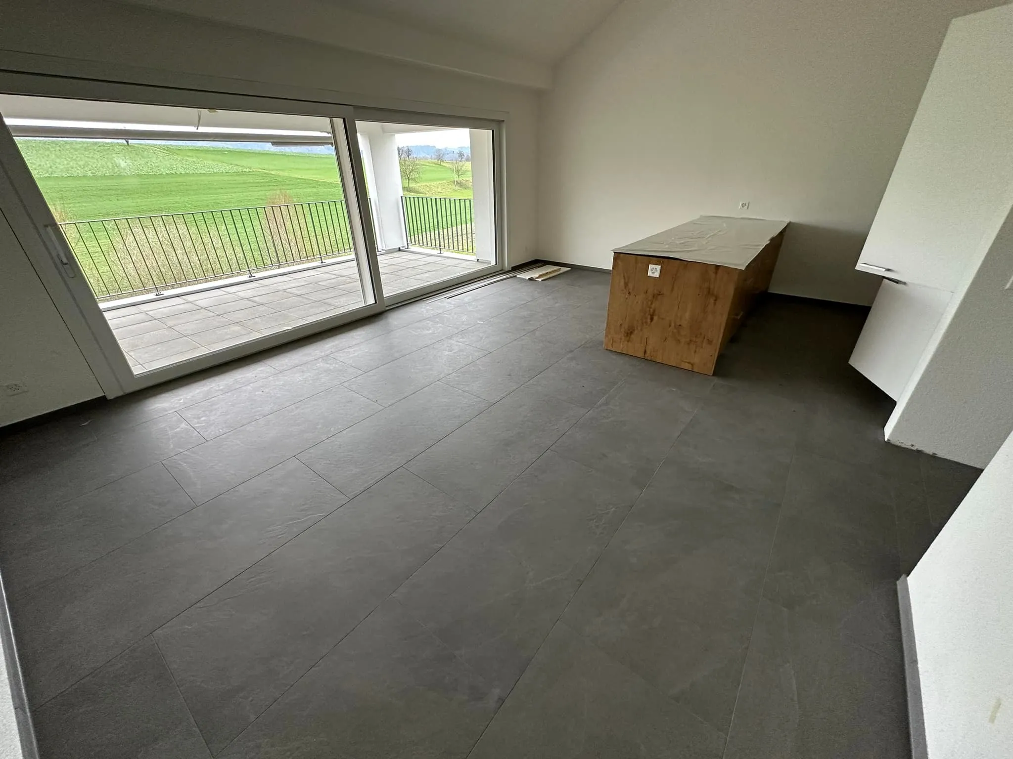 Wohnraum mit dunklem Plattenboden und Schiebefenster zum Balkon.