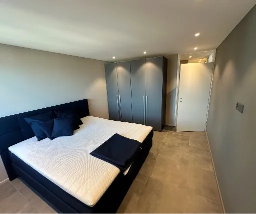 Schlafzimmer mit Plattenboden, Einbauspots und dunkler Akzentwand.