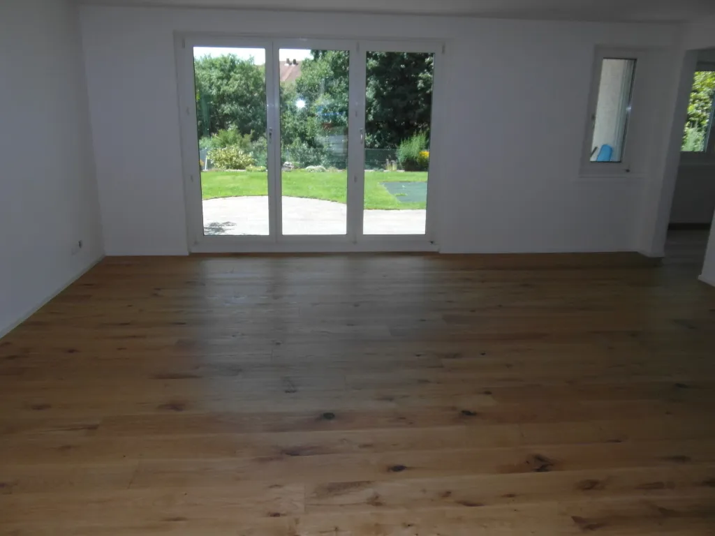Heller Wohnraum mit Landhausdielen und Fenstertür zum Garten.