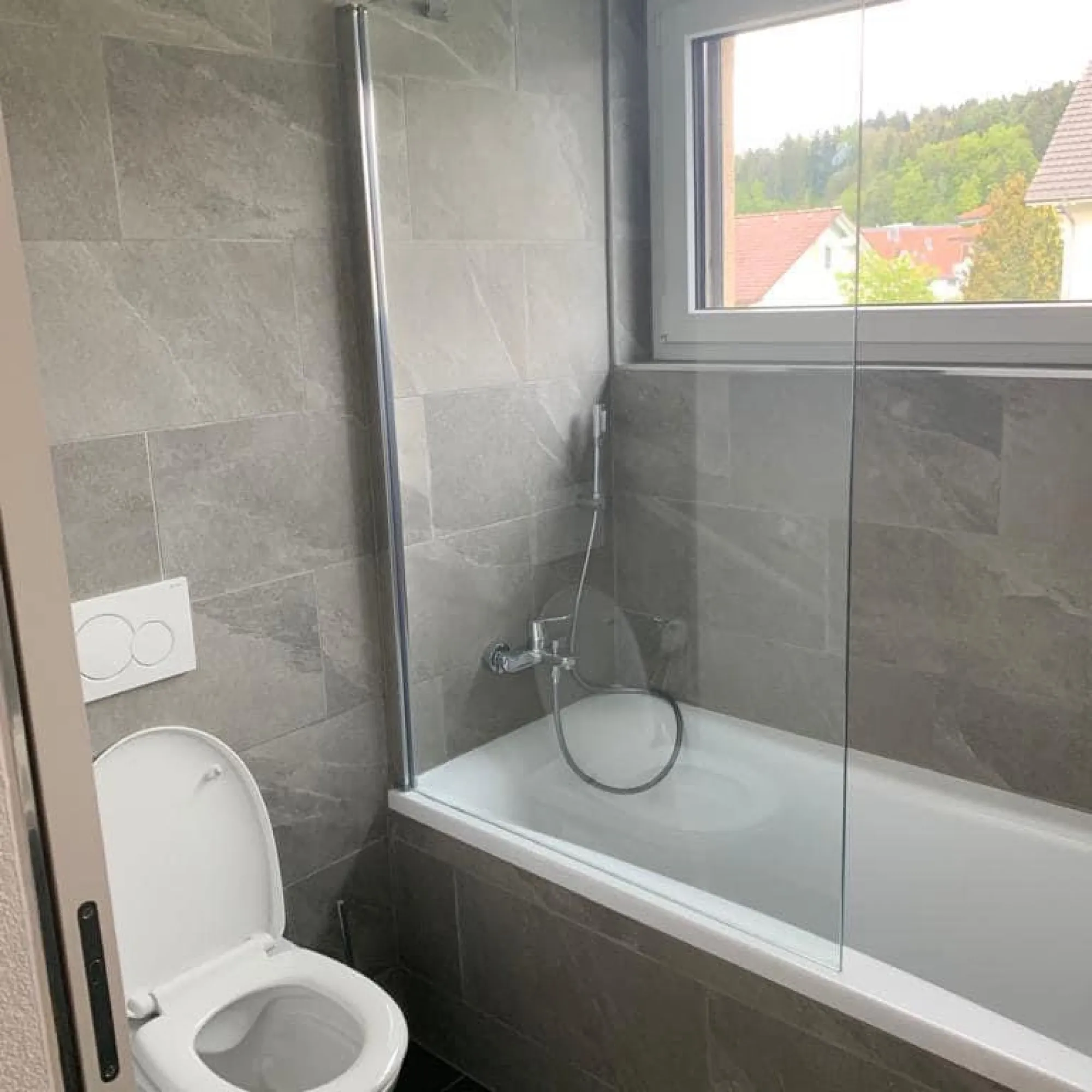 Badewanne mit Glasfaltwand und grauen Platten in Natursteinoptik.