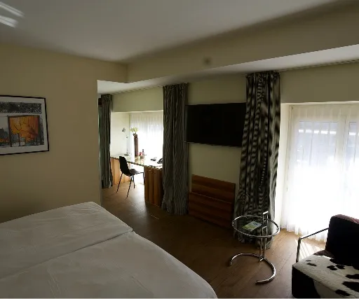 Renoviertes Hotelzimmer mit Holzboden, hellen Wänden und Sitzbereich.