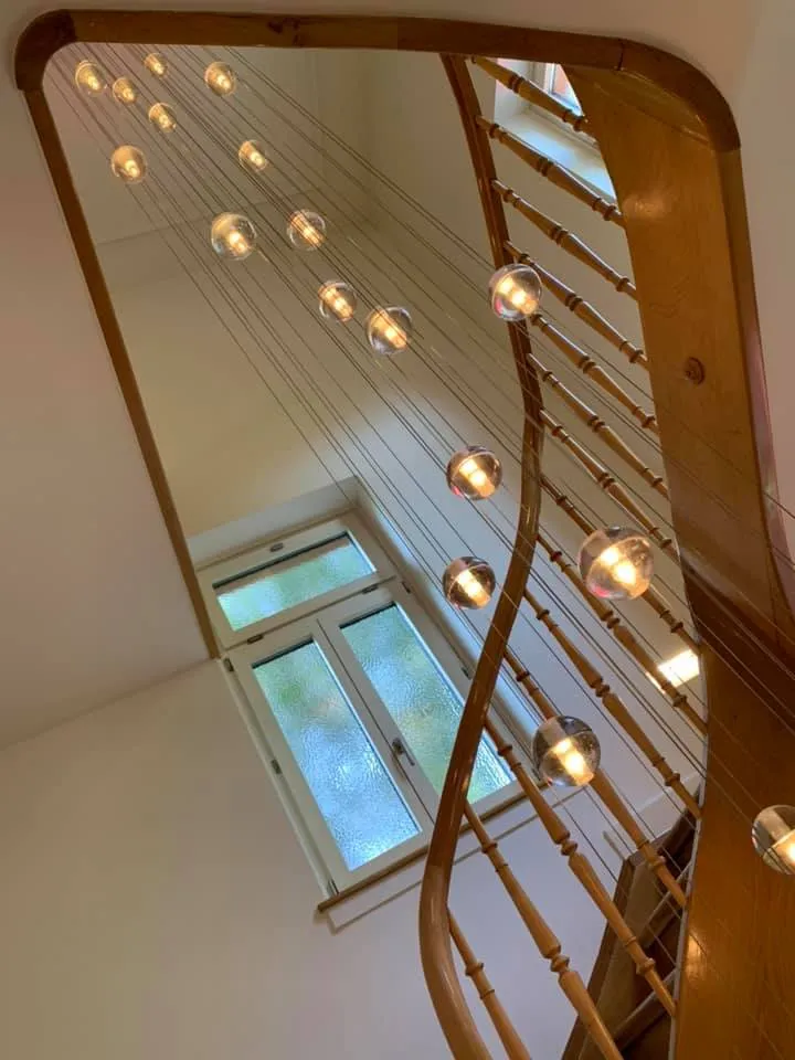 Treppenauge mit geschwungenem Holzhandlauf und hängender Lichtinstallation.