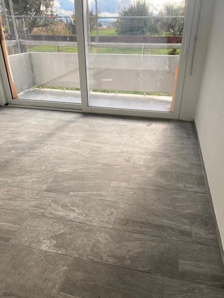 Leerer Raum mit neuem Plattenboden und Fenstertür zum Balkon.