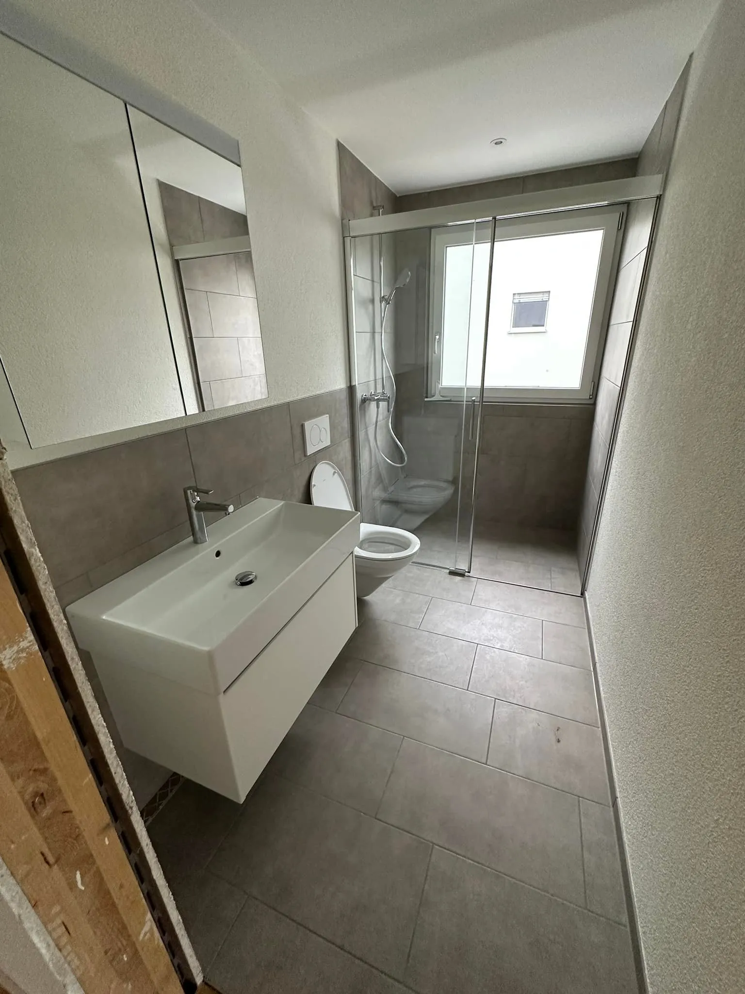 Schmales Duschbad mit bodenebener Glasdusche und grauen Platten.