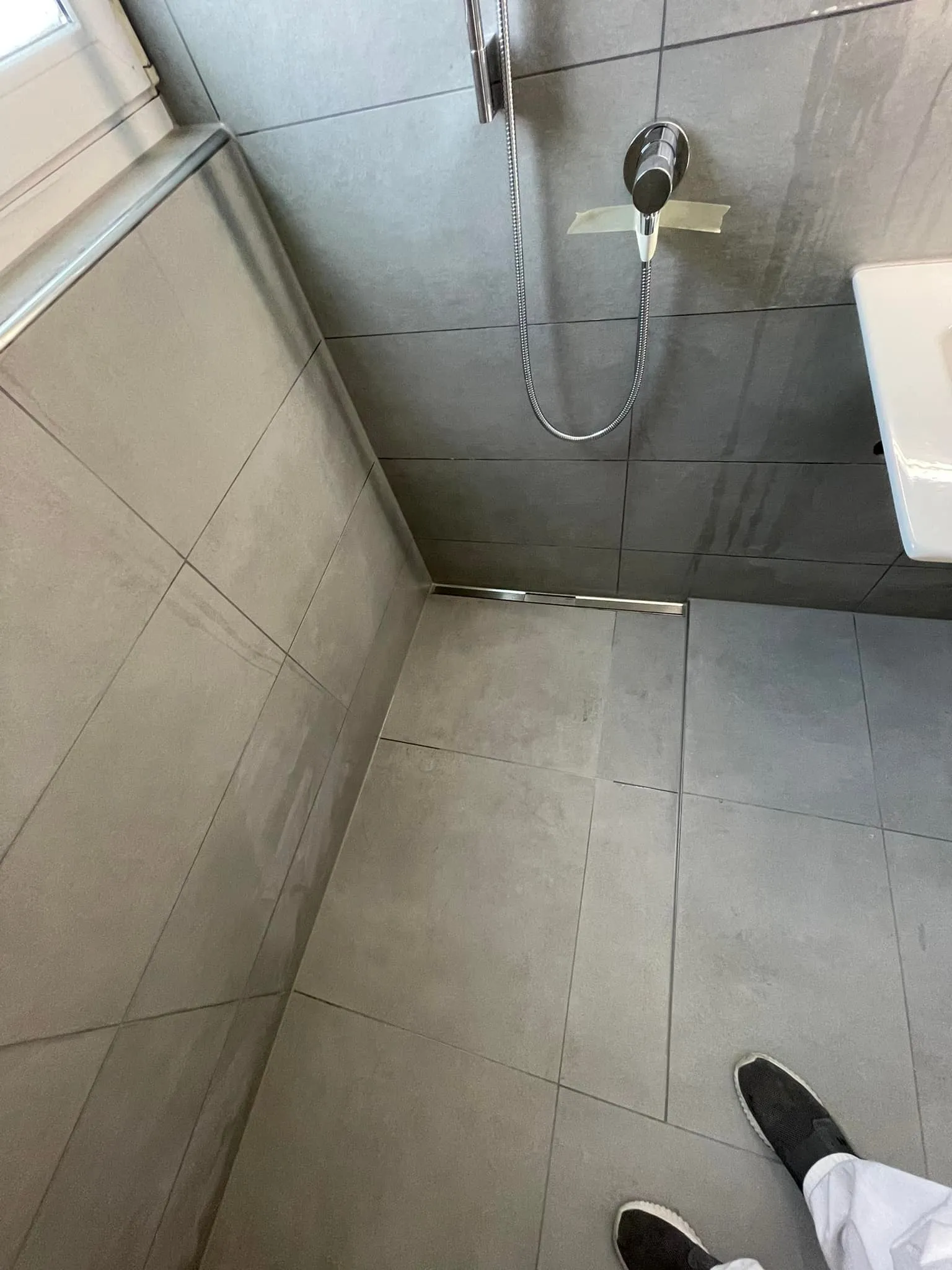 Bodenebene Dusche mit Rinne und grauen Grossformatplatten.