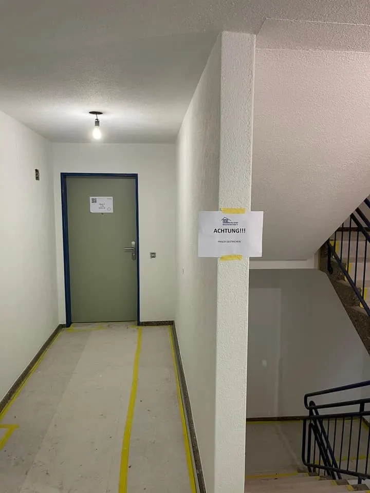 Frisch gestrichenes Treppenhaus mit abgedecktem Boden und Hinweisschild.