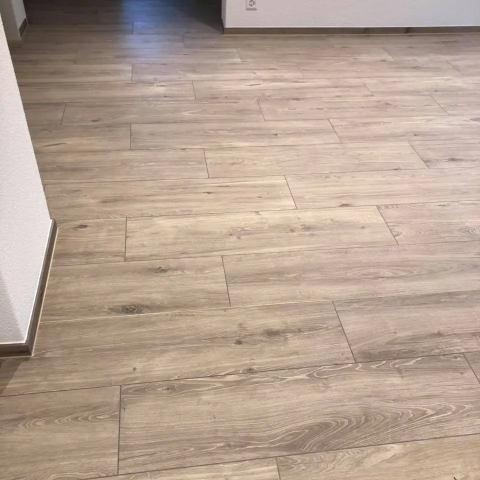 Nahaufnahme des neu verlegten Bodenbelags in Holzoptik mit Sockelleiste.