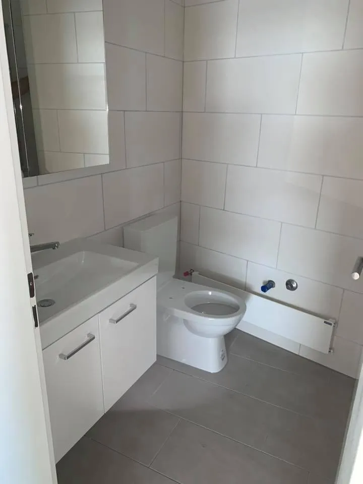 Neues Bad mit grossformatigen Wandplatten und dunklem Plattenboden kurz vor Abschluss.