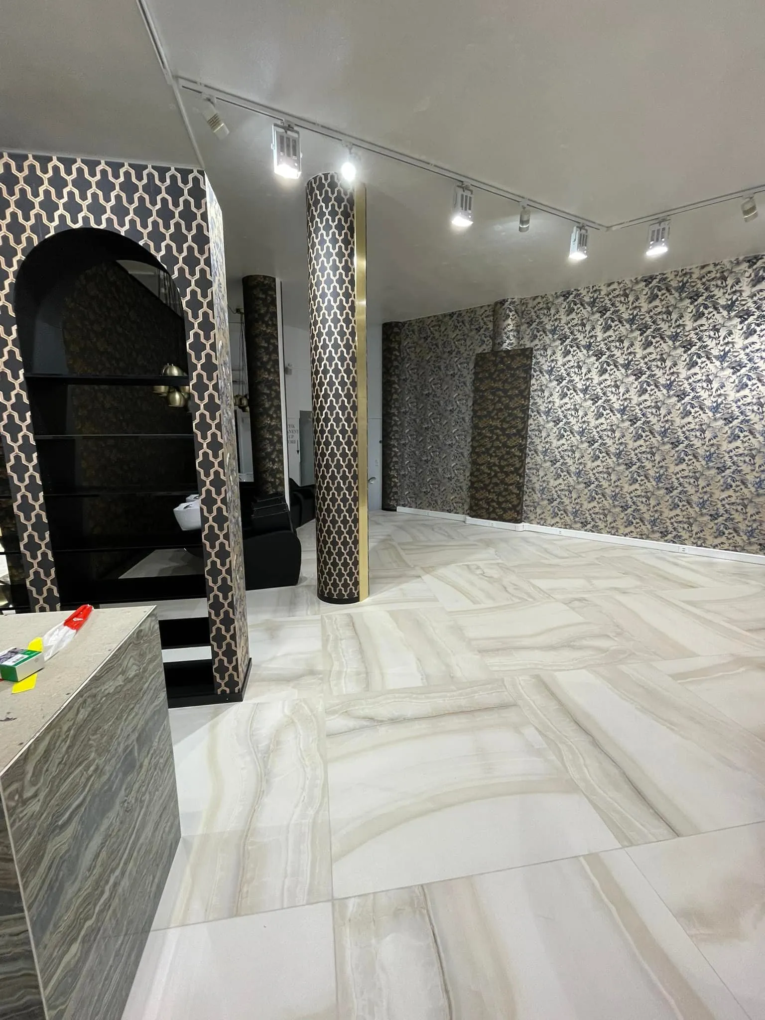 Salonbereich mit tapezierten Säulen, Rundbogenregal und Plattenboden.