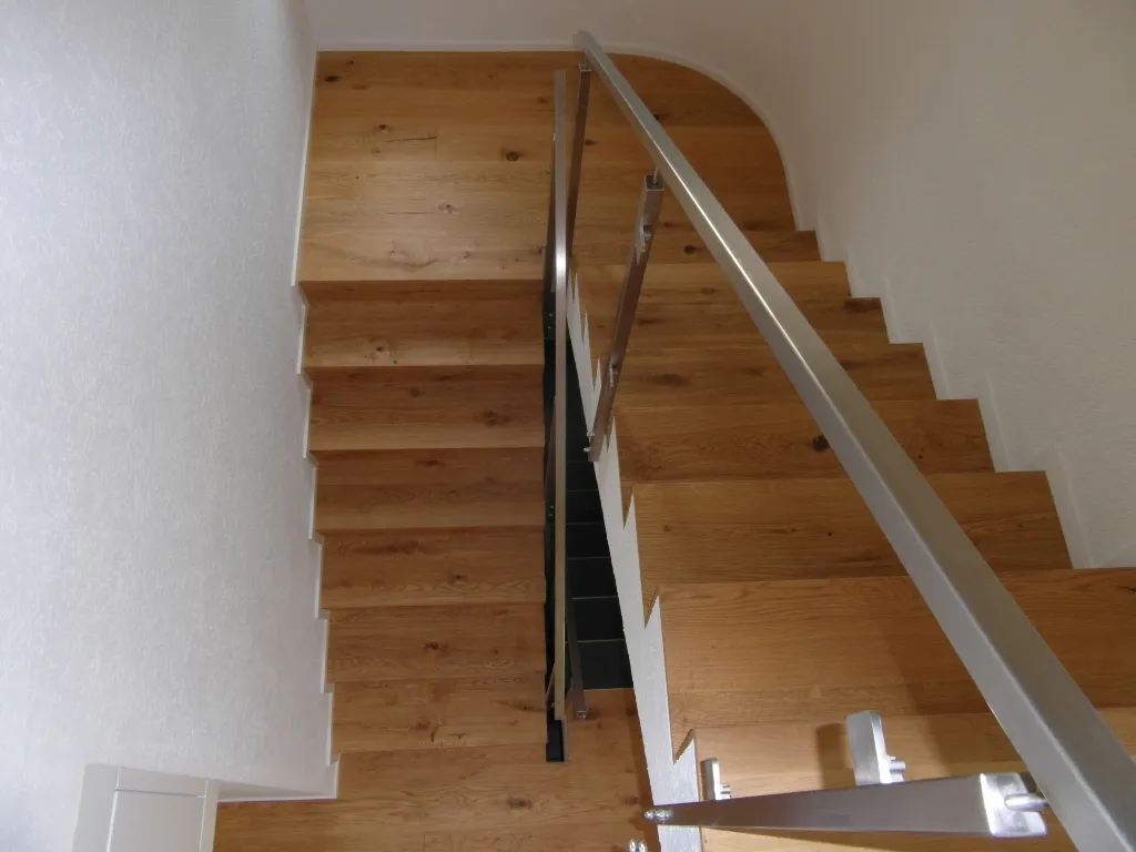 Holztreppe mit Metallhandlauf von oben gesehen.