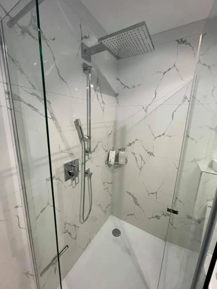 Rahmenlose Glasdusche mit Wandplatten in Marmoroptik.