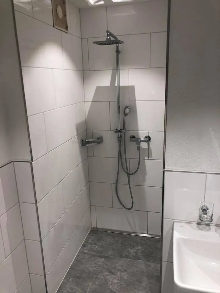 Bodenebene Dusche mit Rinne, weissen Wandplatten und Regenbrause.