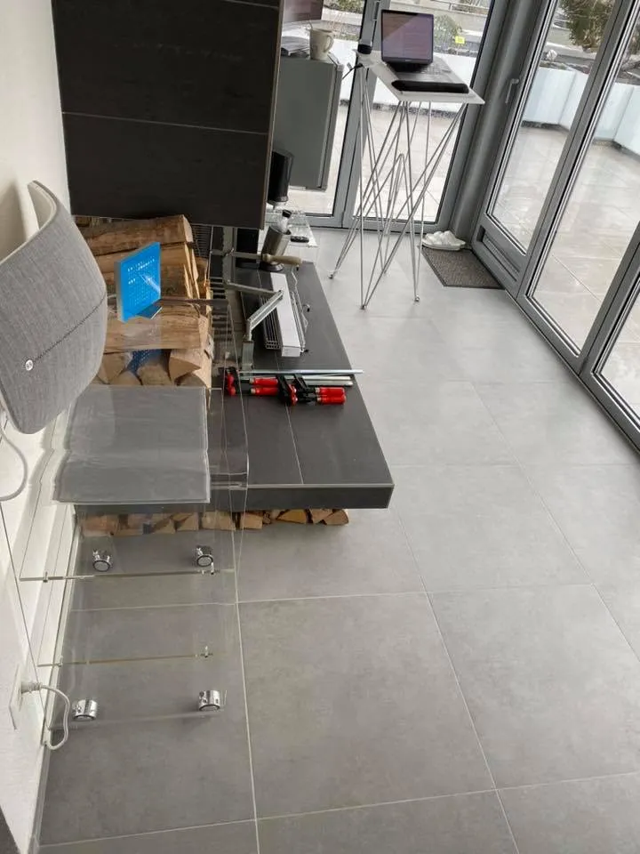 Wohnraum mit grossformatigem grauem Plattenboden und Glasfront.
