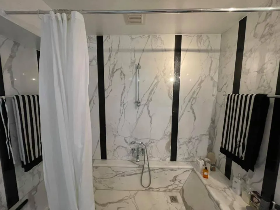 Badewannennische mit Marmoroptik-Platten und schwarzen Wandstreifen.