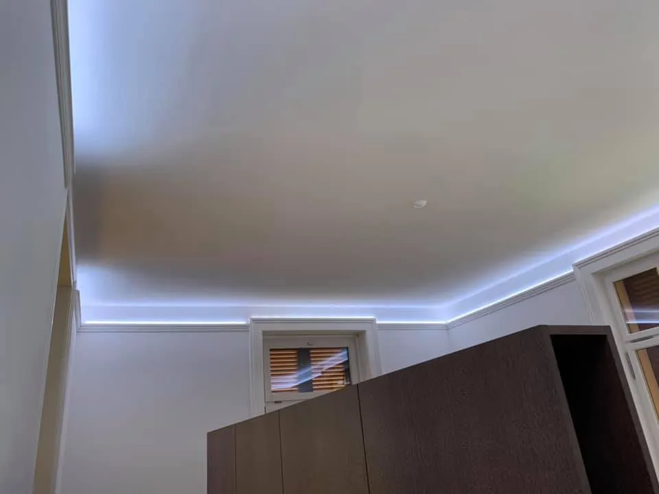 Schlafzimmer mit indirekt beleuchteter Deckenvoute und hellen Wänden.