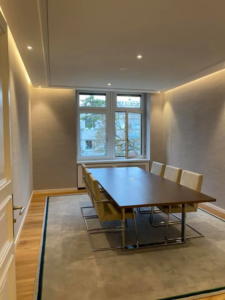 Sitzungszimmer mit indirekt beleuchteter Deckenfuge und aufgearbeitetem Konferenztisch.
