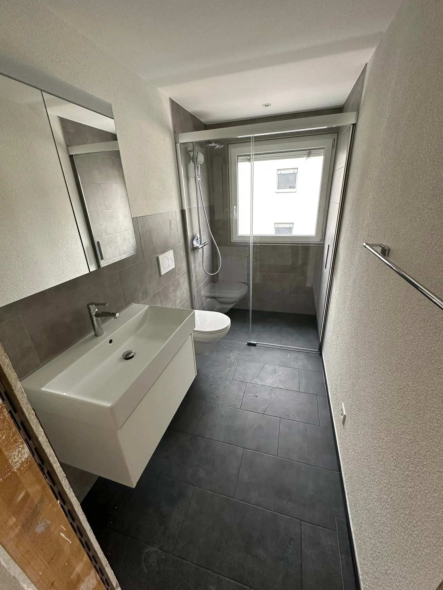 Duschbad mit Glasabtrennung und dunklen grossformatigen Bodenplatten.
