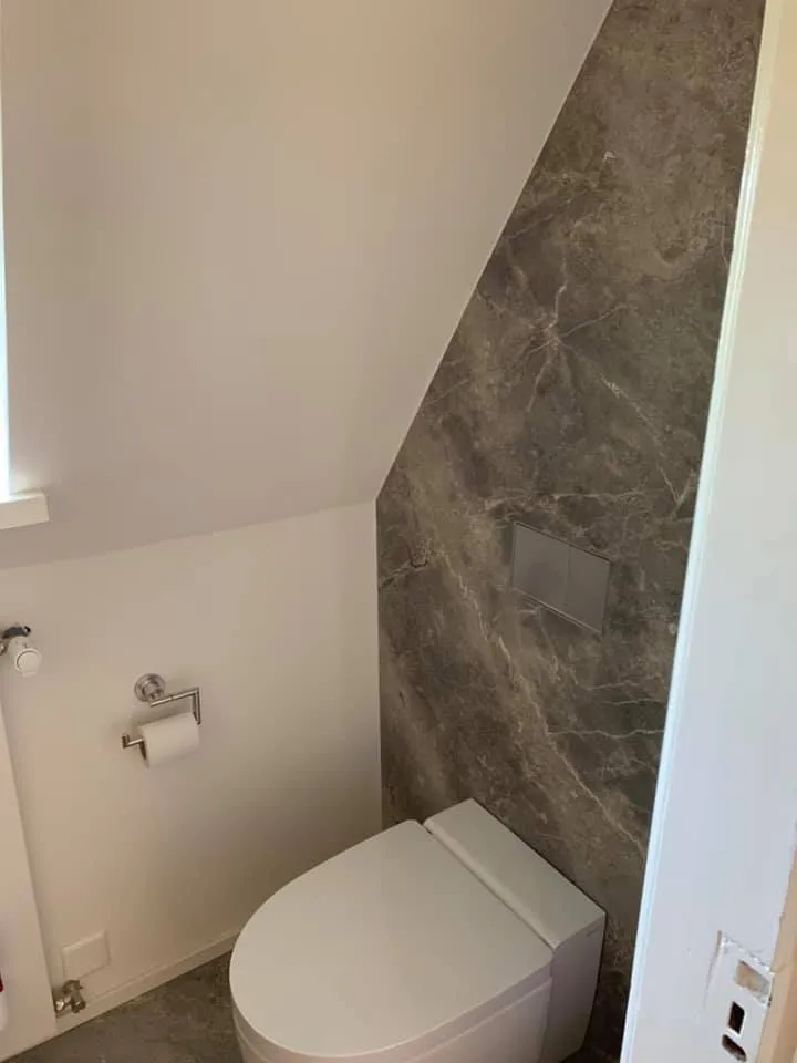 Gäste-WC unter der Dachschräge mit Wandplatten in grauer Marmoroptik.