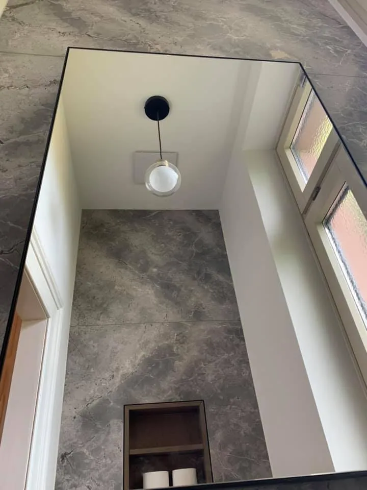 Spiegelung im WC mit grau geplatteter Wand und Pendelleuchte.