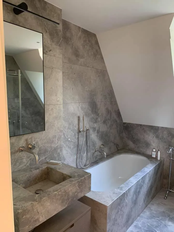 Bad mit verkleideter Wanne und Waschtisch in grauer Marmoroptik.