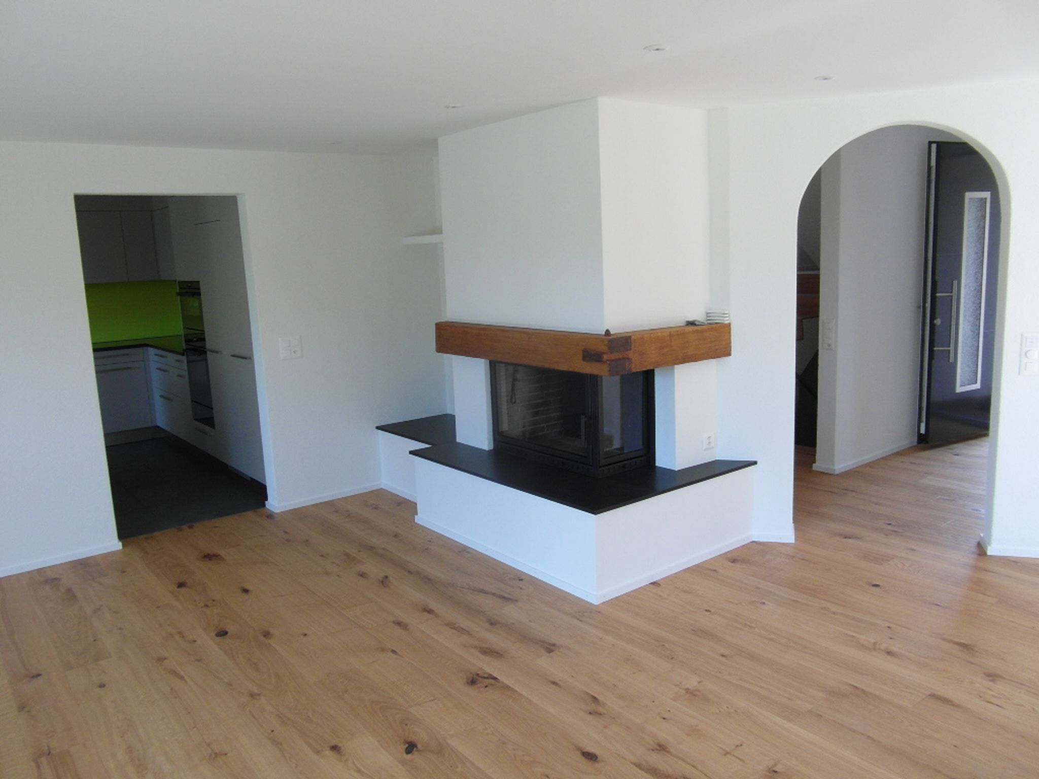Frisch gestrichener Wohnraum mit Cheminée, Rundbogen und Holzboden